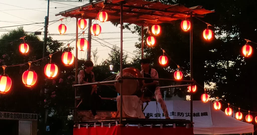 櫓の上で力強く太鼓を叩く男性たちと、それを見上げる来場者たちの様子