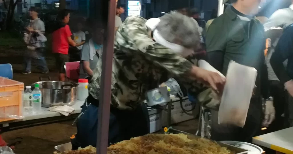 熱気あふれる鉄板の前で気合を入れて焼きそばを振るう屋台の男性
